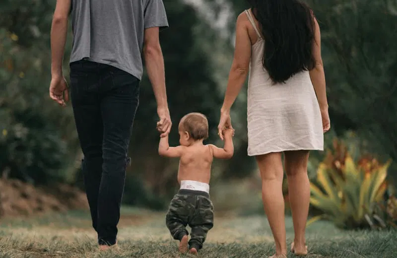 Deux parents tenant la main de leur très jeune enfant