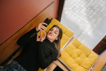 Femme sur son téléphone, allongée sur son canapé